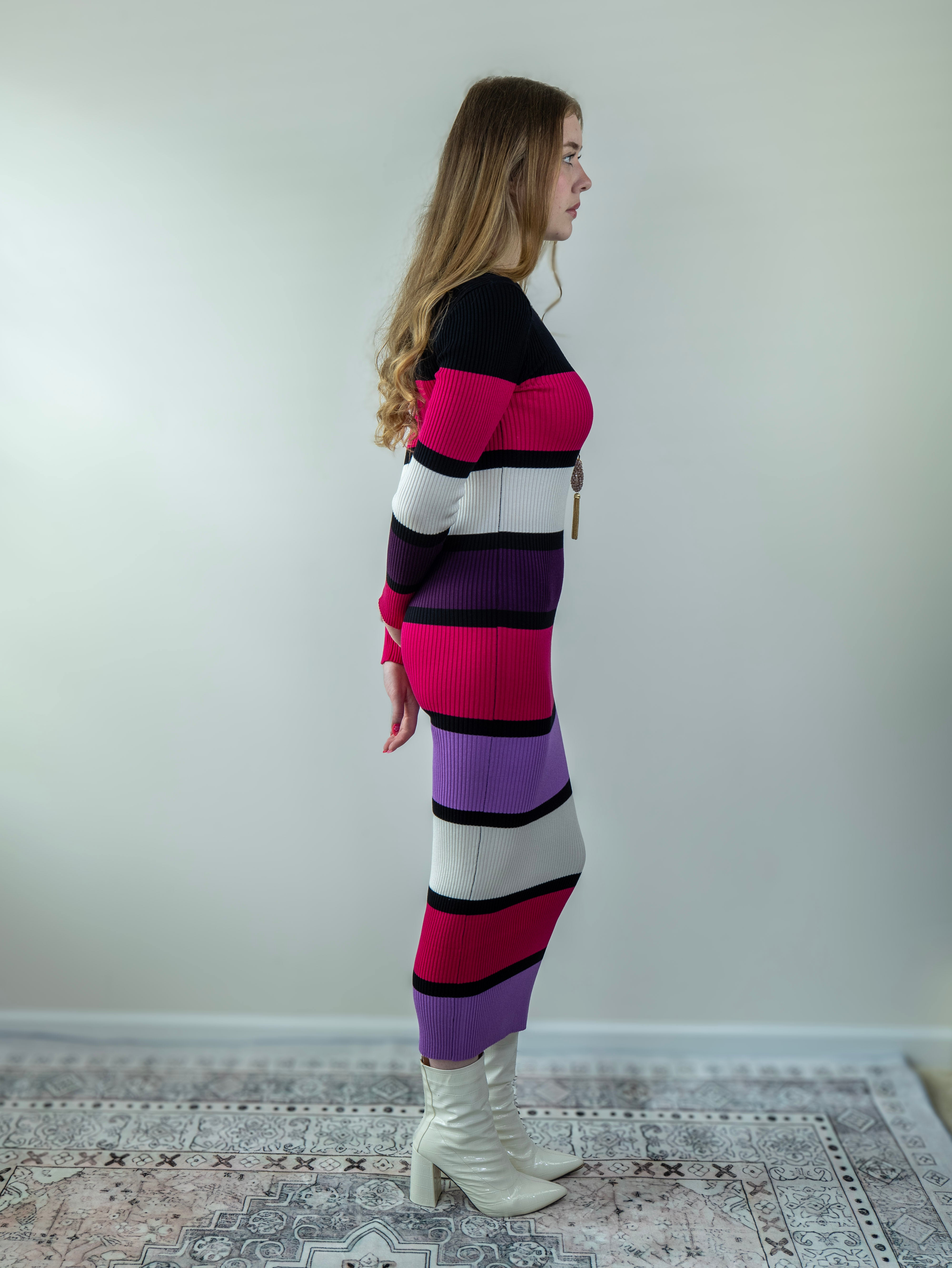 Model wearing a striped midi sweater dress in bold magenta and purple tones, turned slightly to the side.