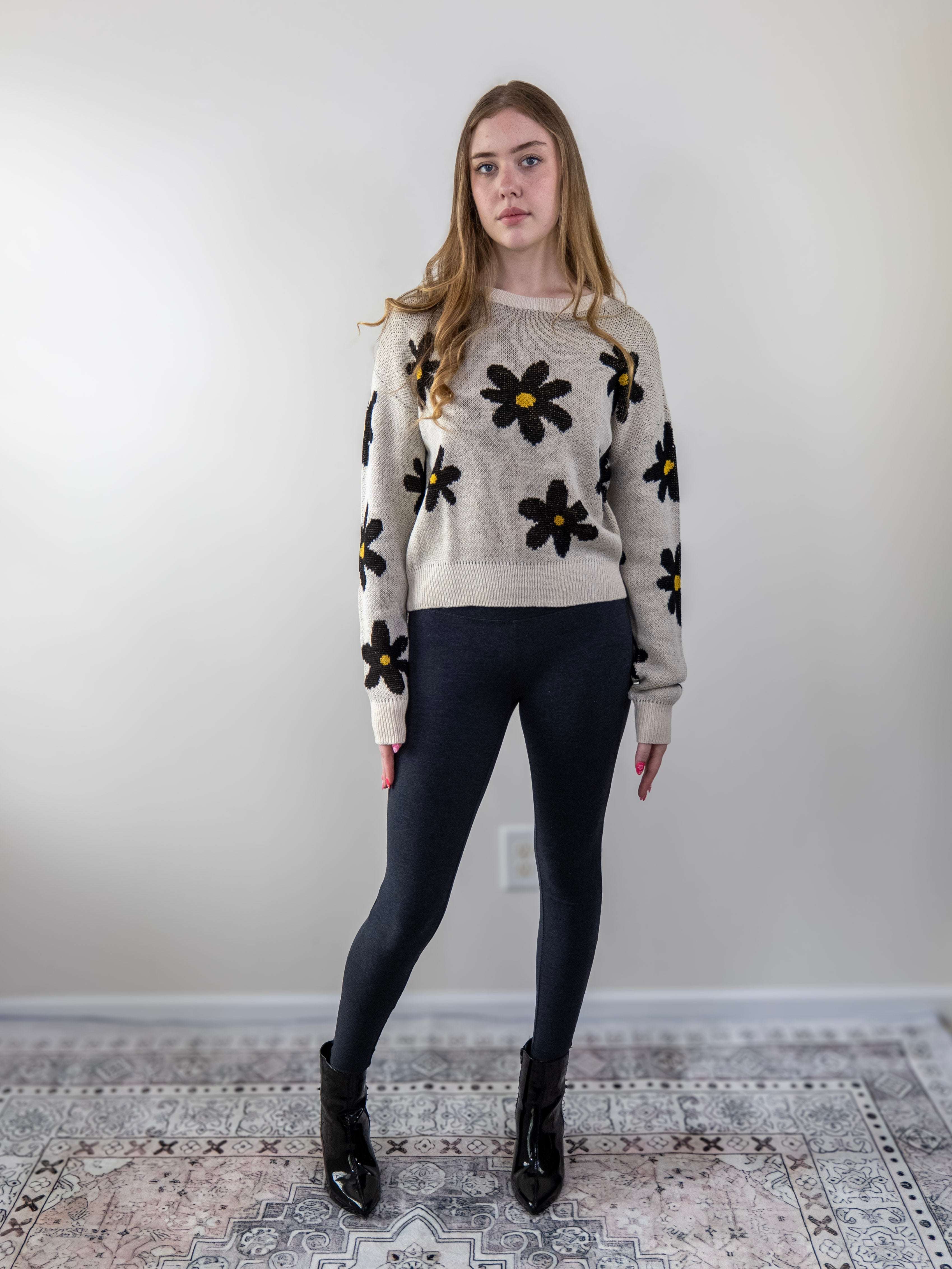 Full-body view of model wearing floral daisy knit sweater with black leggings.