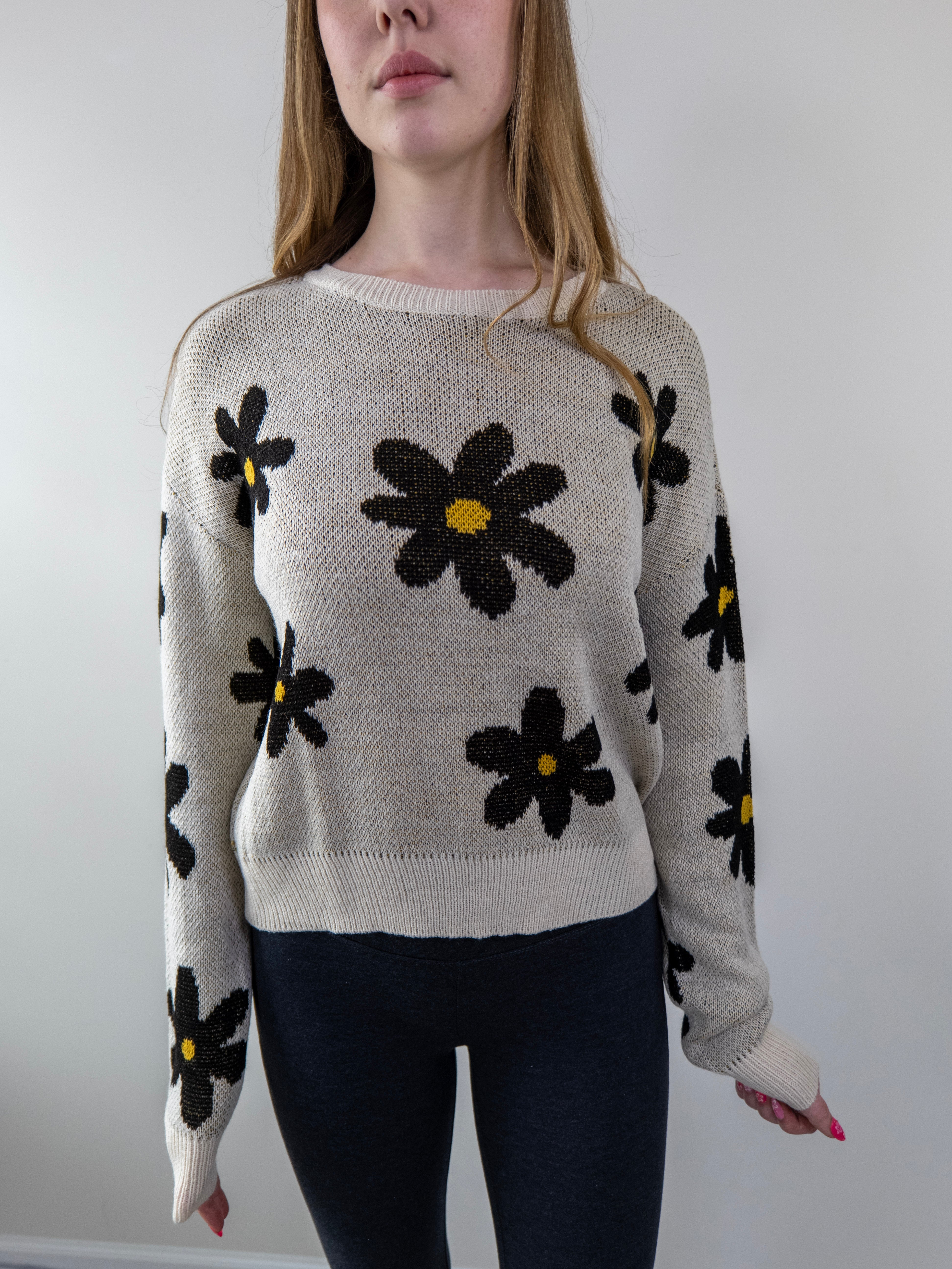 Close-up of daisy floral print and ribbed knit texture on beige sweater.