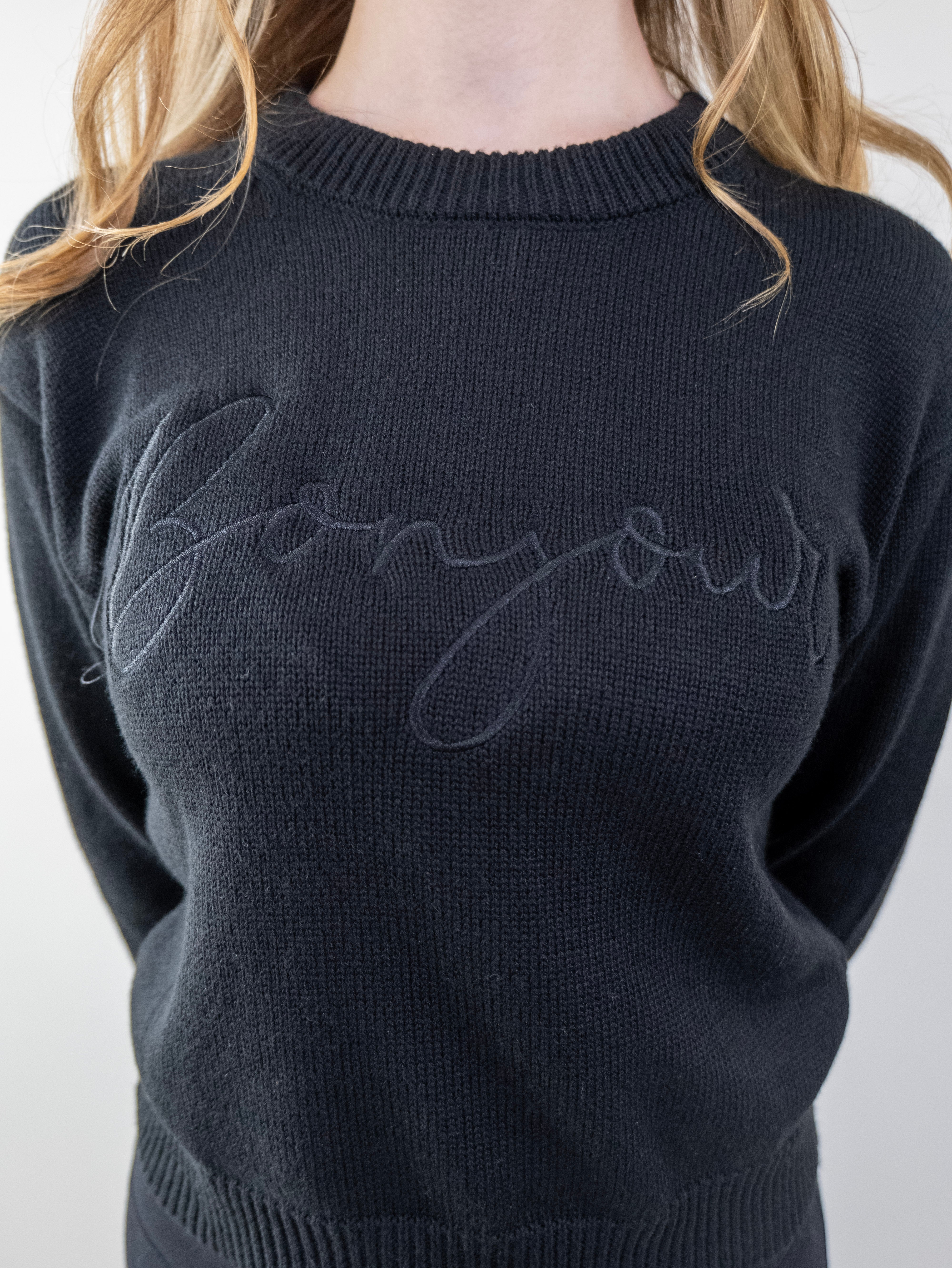Close-up of the “Bonjour” script on the black sweater