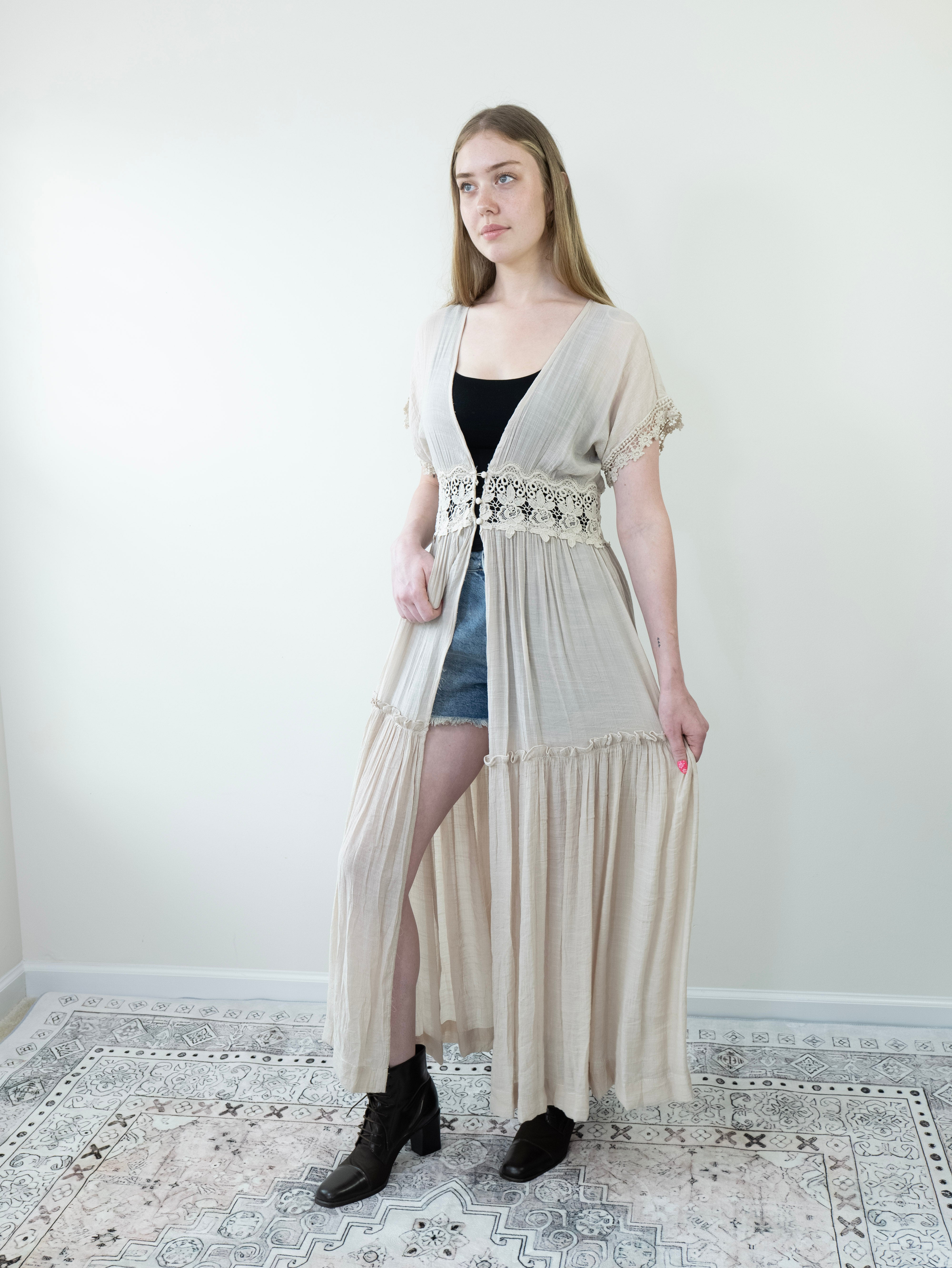 Model wearing beige lace-trim Breeze Maxi Duster, front view black sleeveless tank top, jeans shorts, black ankle patent leather boots.