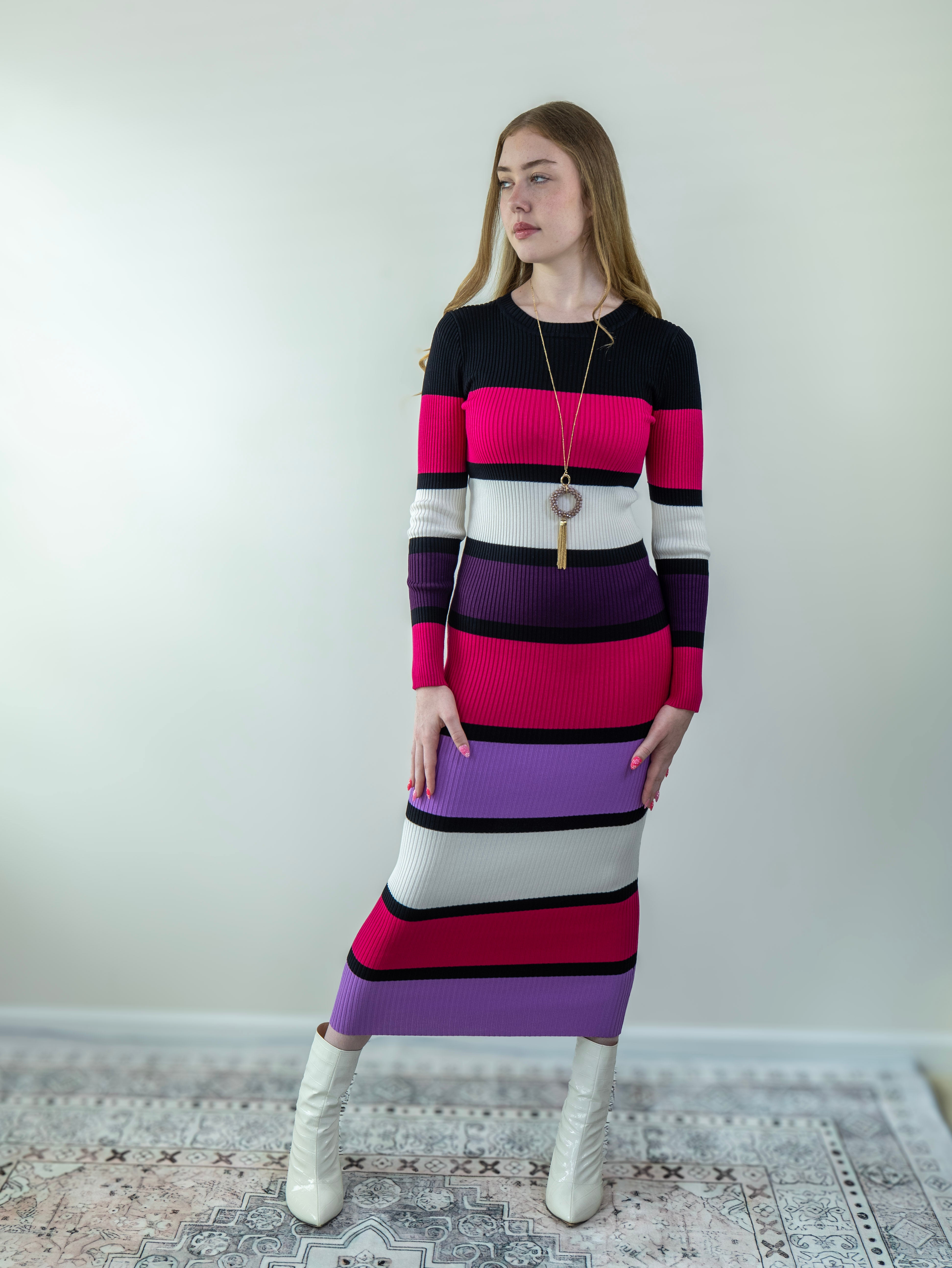 Model wearing a multicolor rib-knit midi sweater dress in magenta, black, purple, and off-white, standing front-facing.