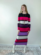 Model wearing a multicolor rib-knit midi sweater dress in magenta, black, purple, and off-white, standing front-facing.