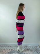 Model wearing a striped midi sweater dress in bold magenta and purple tones, turned slightly to the side.