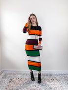 Model wearing orange multi-stripe rib-knit midi sweater dress, standing front view.