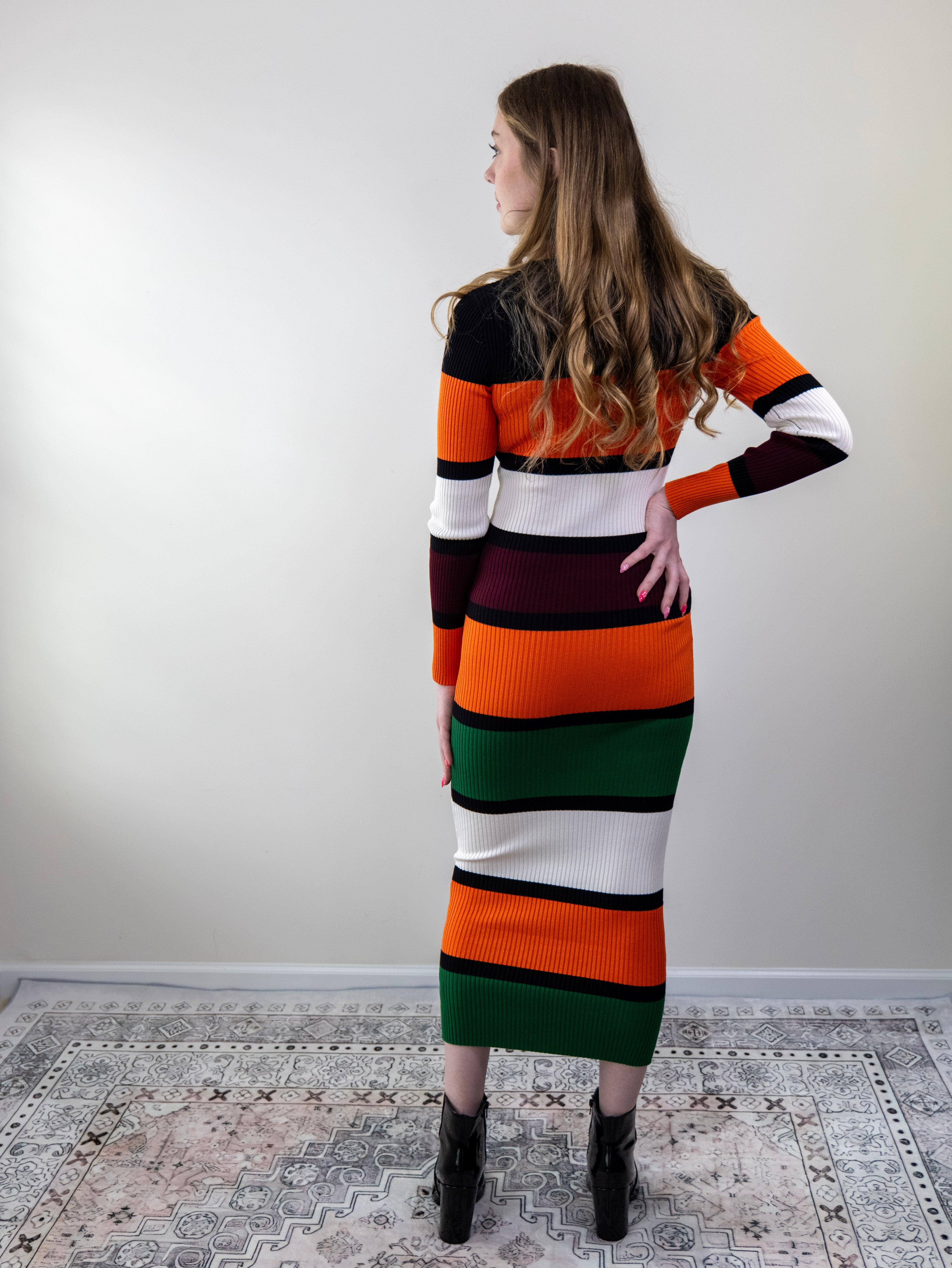 Back view of orange multi-stripe midi sweater dress on model.
