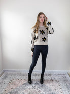 Model wearing beige daisy-print knit sweater with black leggings, front view.