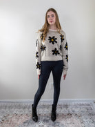 Full-body view of model wearing floral daisy knit sweater with black leggings.
