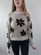 Close-up of daisy floral print and ribbed knit texture on beige sweater.