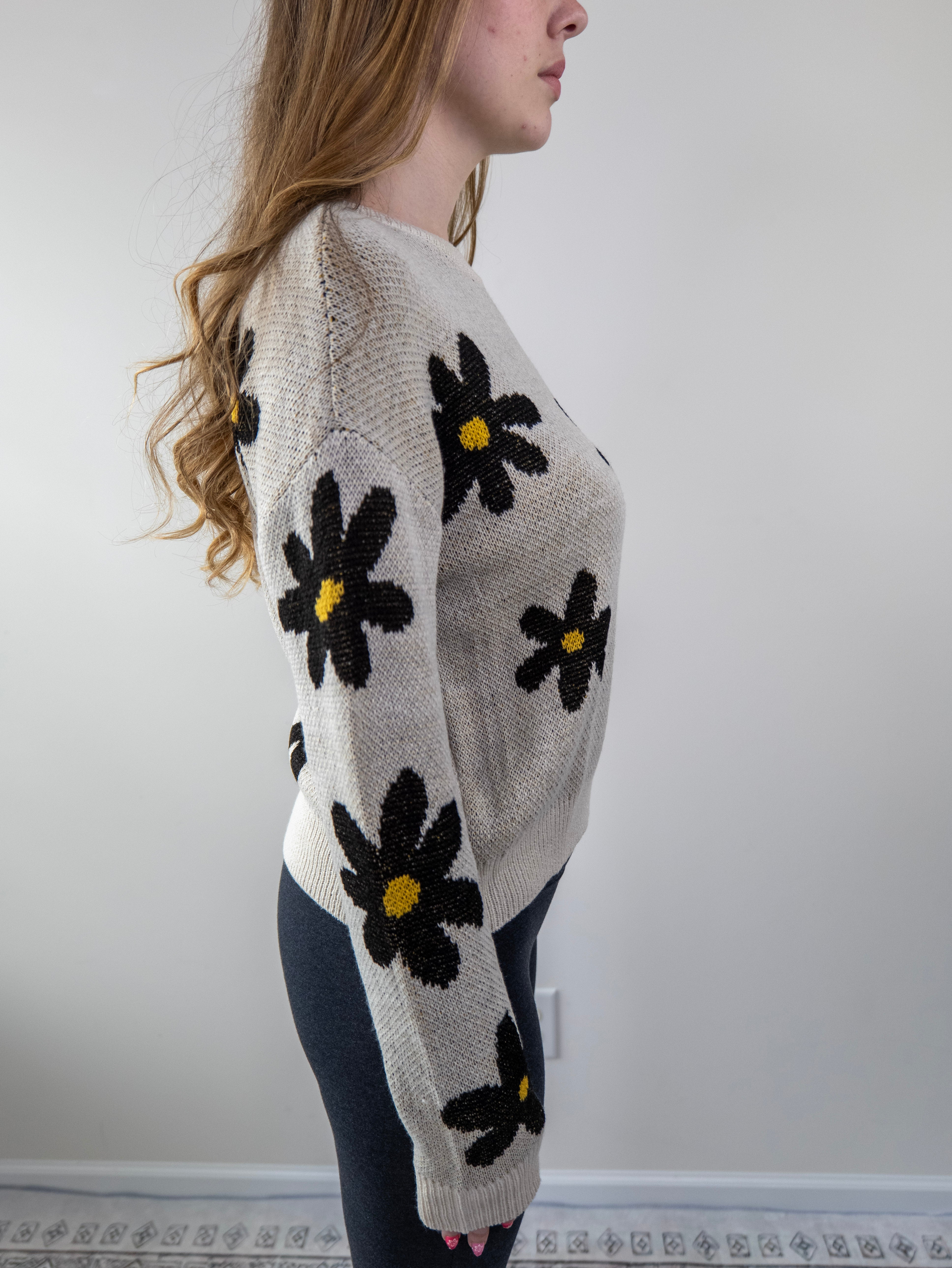 Side view of beige knit sweater with daisy floral print and ribbed cuffs