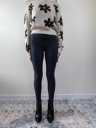 Full-body view of model wearing floral daisy knit sweater with black leggings.