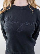 Close-up of the “Bonjour” script on the black sweater