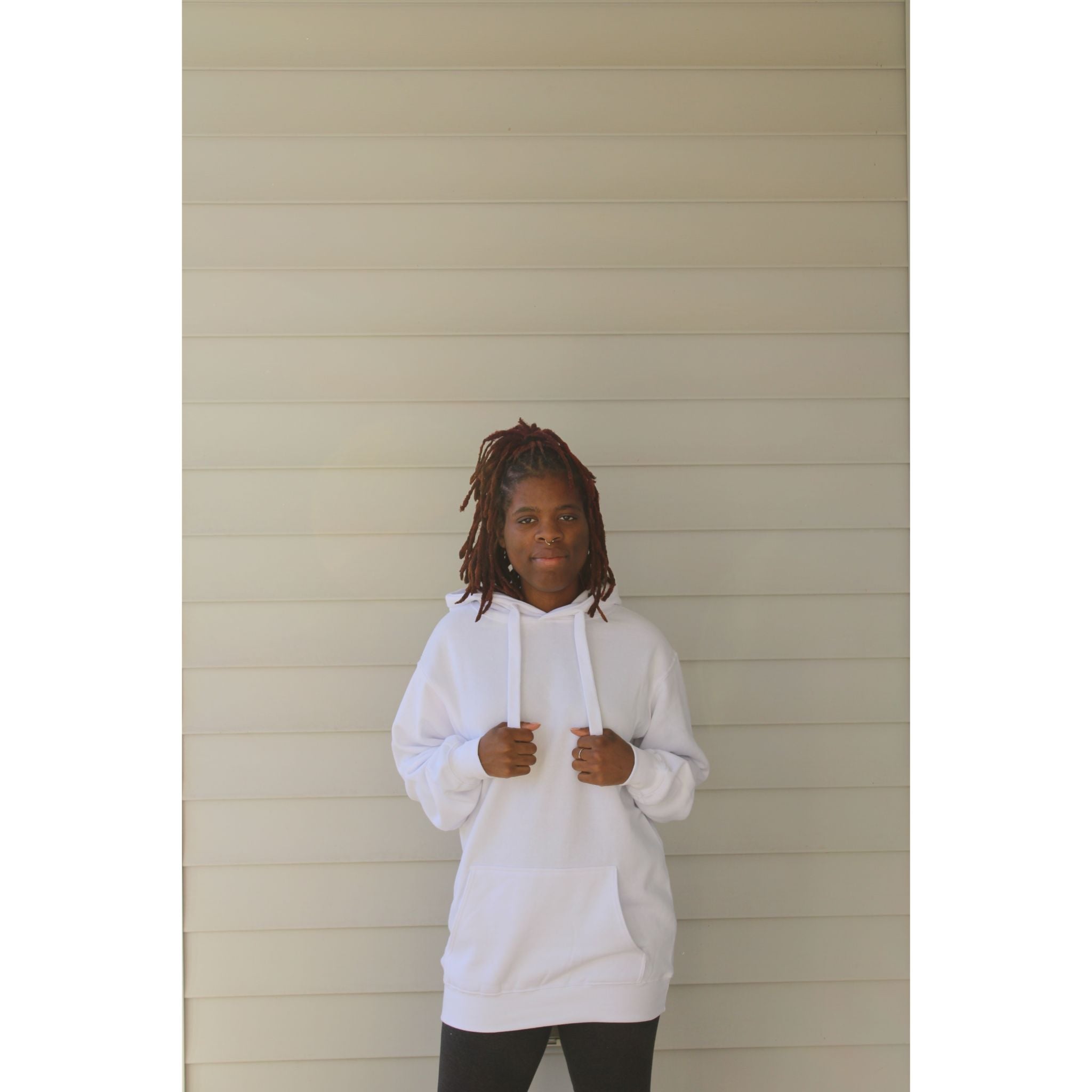 White oversized hoodie with thick drawstring, kangaroo pocket, and long sleeves, made for a cozy and relaxed fit. Model showing the front holding the drawstring.