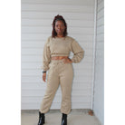 Khaki two-piece sweatsuit set with a long-sleeve crop top and pull-on pants featuring a drawstring waist and elastic ankle cuffs, designed for all-day comfort. Model standing showing the set